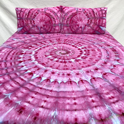 Pink tie-dye bedspread with matching pillows on a white background